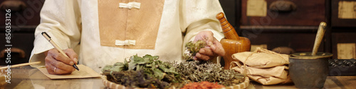 Fotografie Apothecary in traditional clothes making recipe from dried herbs in drug store