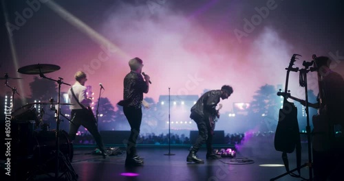 Rock Music Concert at a Festival: Energetic Indie Band Performs Live on Open Air Stage at Sunset, Using Instruments to Play Indie, Punk, and Alternative Tunes. Cinematic Footage From the Back photo