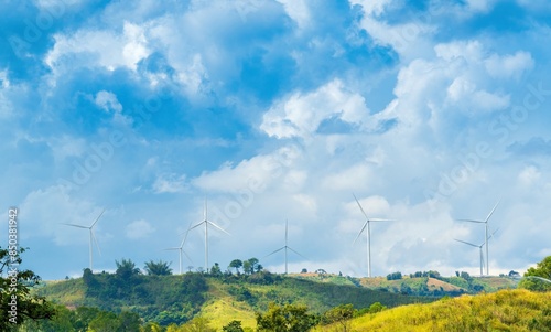 Wind turbines stand tall on lush green hills beneath a bright blue sky full of clouds, perfect for promoting environmental awareness or green energy initiatives.