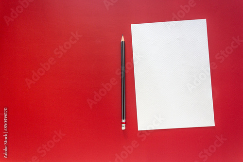 A crisp white sheet of paper and a black wooden pencil rest on a bold red background for concepts related to education, creativity, writing, and design.