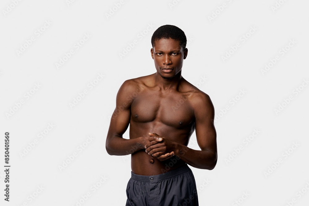 African American man stands confidently with no shirt against a stark white backdrop in a studio setting. African American man stands confidently with no shirt against a stark white backdrop in a studio setting.