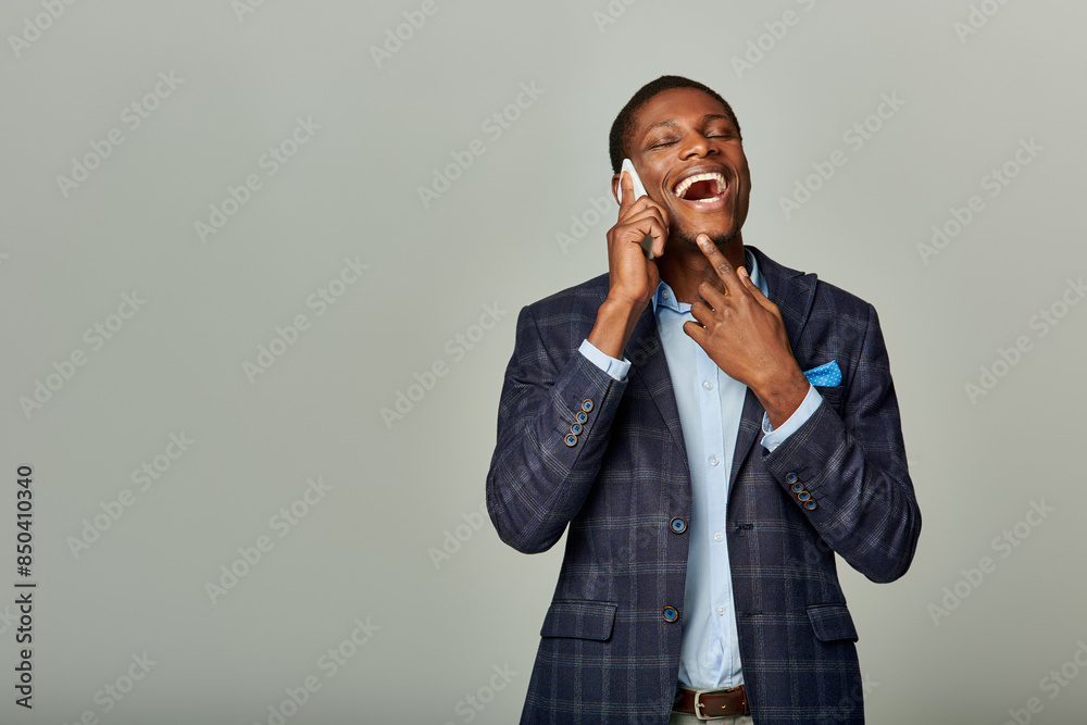An African American businessman in a checkered blazer suit talking on a cellphone against a grey backdrop. An African American businessman in a checkered blazer suit talking on a cellphone against a grey backdrop.