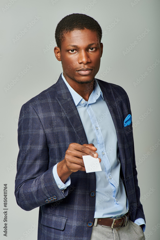 African American businessman in stylish suit presenting a business card against a grey backdrop. African American businessman in stylish suit presenting a business card against a grey backdrop.