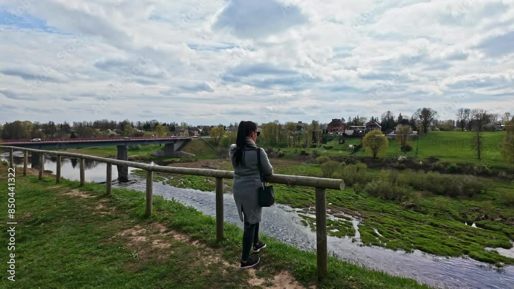 Young woman with black hair looking at small river water stream near bridge Young woman with black hair looking at small river water stream near bridge