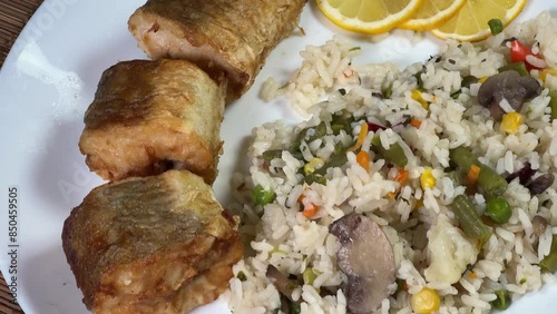 Fried hake hubbsi pieces with rice and vegetables, top view photo