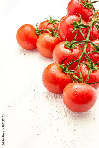Ripe cherry tomatoes with water drops on white wooden surface in the upper right corner of the photo. Vertical orientation of the photo. Close-up of cherry tomatoes.