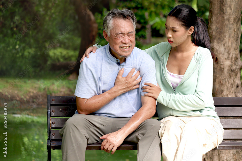 Fototapeta premium Elderly Asian man experiencing a heart attack during take a walk in park with daughter. Teenage girl help senior grandpa who has cardio problems chest pain while rest on bench in outdoors green garden