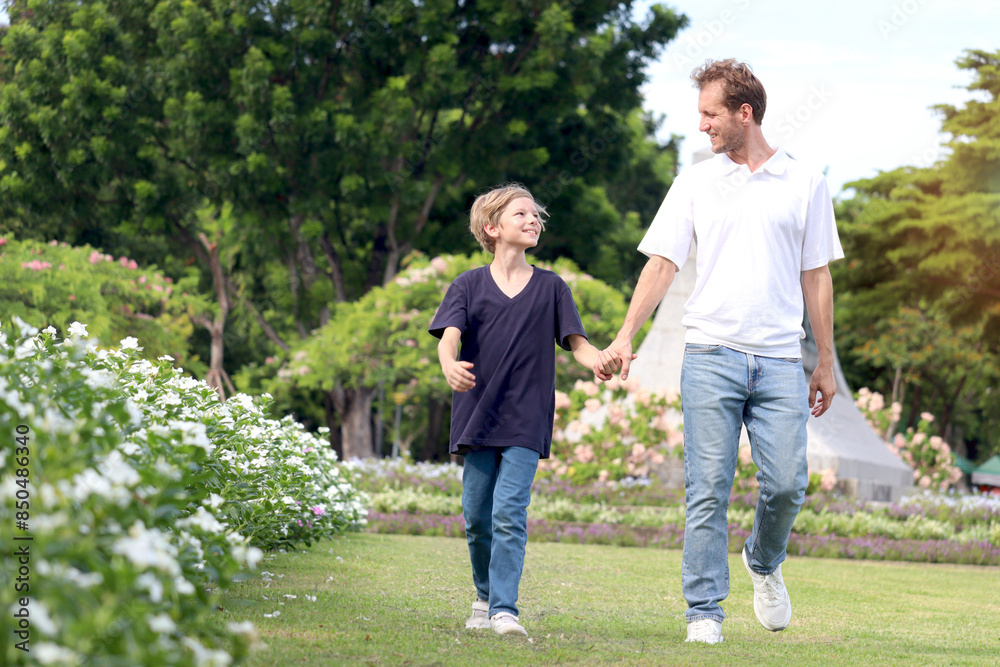 Father and son holding hands while walking in the park. Happy family, parent and kid spending time outdoors together in beautiful garden on holiday. little boy child playing with father outside. Father and son holding hands while walking in the park. Happy family, parent and kid spending time outdoors together in beautiful garden on holiday. little boy child playing with father outside.