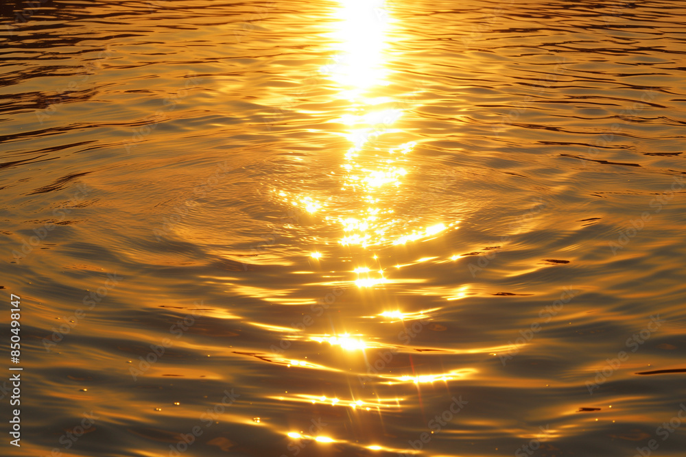Ripples on surface of golden water with rising sun glow brightly shining through.
Ripples on surface of golden water with rising sun glow brightly shining through.