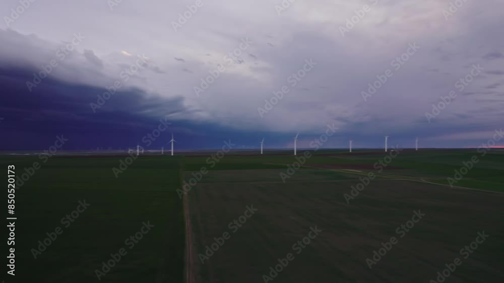 Wind turbines on a vast green field under a dramatic stormy sky at dusk Wind turbines on a vast green field under a dramatic stormy sky at dusk