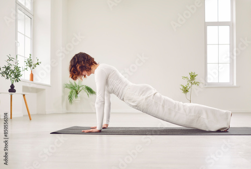 Yogi attractive sporty woman working out in white studio, side view portrait of model doing exercise on mat. Standing in plank pose, phalankasana, home sport fitness for wellness, weight loss, fitness photo