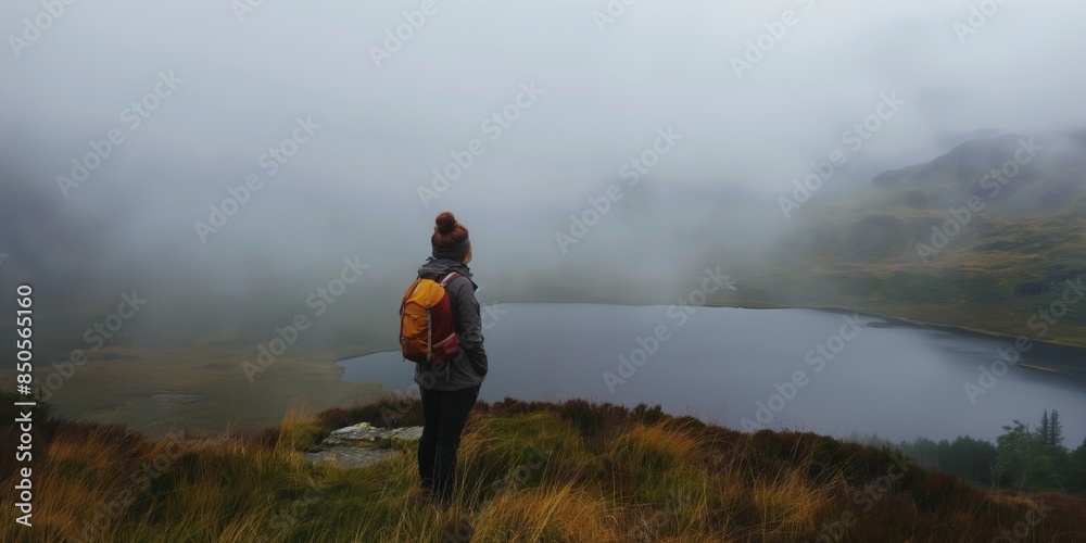 A person with a backpack stands overlooking a foggy lake in a serene mountainous landscape. A person with a backpack stands overlooking a foggy lake in a serene mountainous landscape.