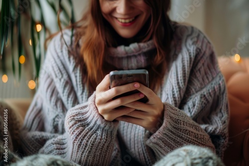 A happy young woman, sitting at home on the couch using her smartphone, smiling and looking at the screen while shopping online or working on social media apps. Social concepts, lifestyle