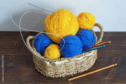Knitting concept. Balls of wool, knitting needles and crochet hooks in small basket on dark rustic table. Copy space
