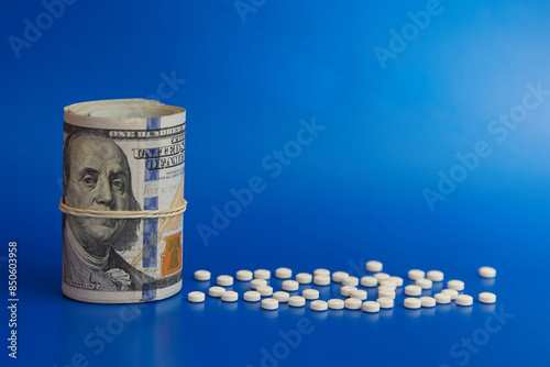 A twisted pack of hundred dollar bills and a money rubber band covering Franklin's mouth on a blue background, white pills and dollars, truth about drugs, side effects of drugs, placebo for money photo