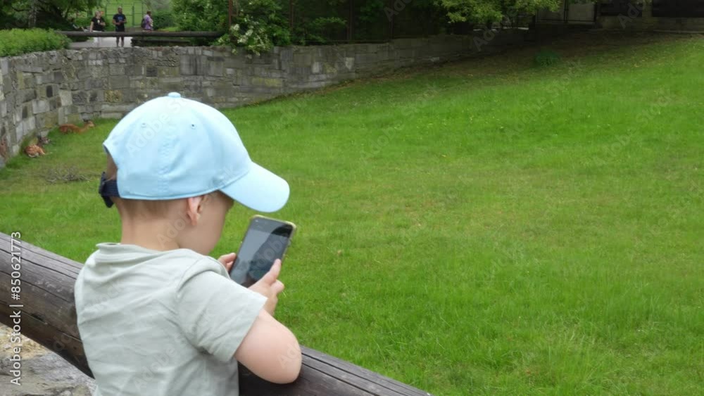 Little boy at the zoo takes pictures of the animals with his cell phone. Rest in the zoo. Time with family. Little boy at the zoo takes pictures of the animals with his cell phone. Rest in the zoo. Time with family.