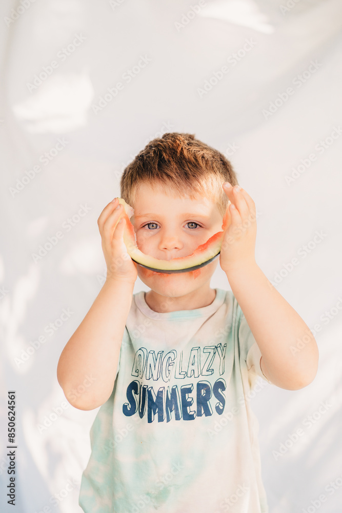 Young boy sitting in a field on a summers day eating watermelon