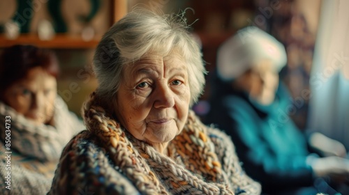 Elderly lady in a knitting circle, pausing due to shoulder pain, other members in soft focus, warm homely atmosphere --ar 16:9 Job ID: 3e76587f-4128-453c-9ee5-5fa2fead2504