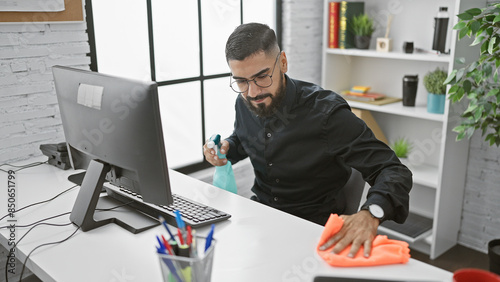 Canvas Print Handsome man cleaning office desk with spray and cloth, maintaining hygiene in workplace setting