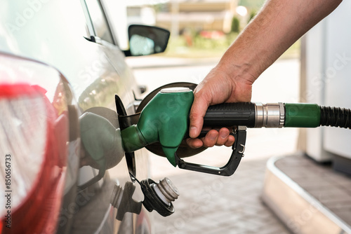 Close-up of a hand refueling a car with a green nozzle at a gas station