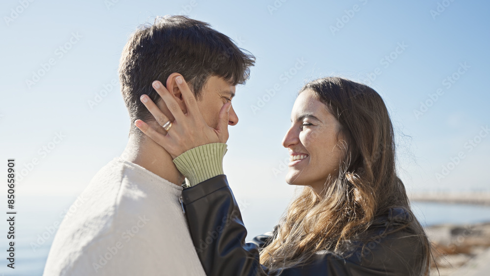 A couple exhibits love and togetherness by the sea, with the woman and man closely embracing in a serene outdoor beach setting.