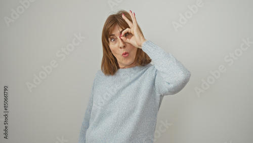 Mature woman making ok sign over eye against white background, expressing positivity and humor.