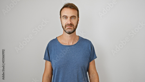 Obraz na plátně Portrait of a handsome middle-aged hispanic man with a beard, wearing a casual t-shirt against a white background