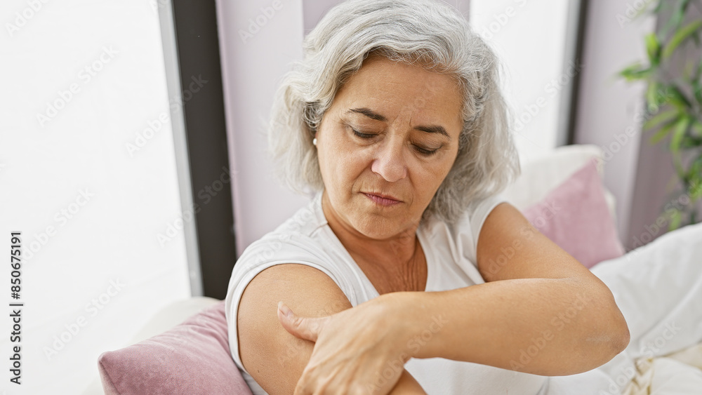 Mature woman applies lotion in a cozy bedroom setting, exuding self-care and comfort. Mature woman applies lotion in a cozy bedroom setting, exuding self-care and comfort.