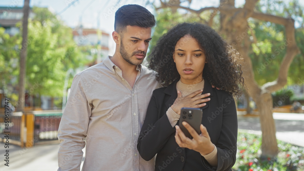 A concerned couple examines a smartphone together in a green park setting, symbolizing connection and outdoor technology use. A concerned couple examines a smartphone together in a green park setting, symbolizing connection and outdoor technology use.