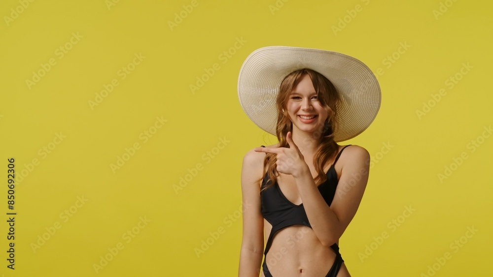 Young woman in swimsuit and stylish hat smiling pointing finger at empty area. Travel, summertime vacation, beach leisure concept. Young woman in swimsuit and stylish hat smiling pointing finger at empty area. Travel, summertime vacation, beach leisure concept.