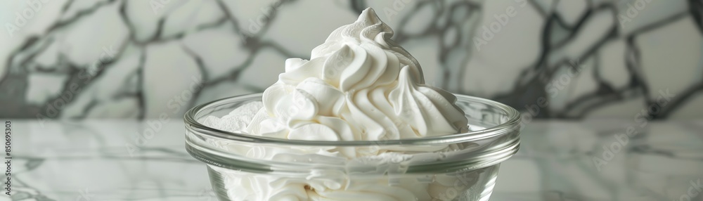 Perfectly beaten egg whites forming soft peaks in a clear glass bowl, with a mixer visible on a pristine marble surface Perfectly beaten egg whites forming soft peaks in a clear glass bowl, with a mixer visible on a pristine marble surface