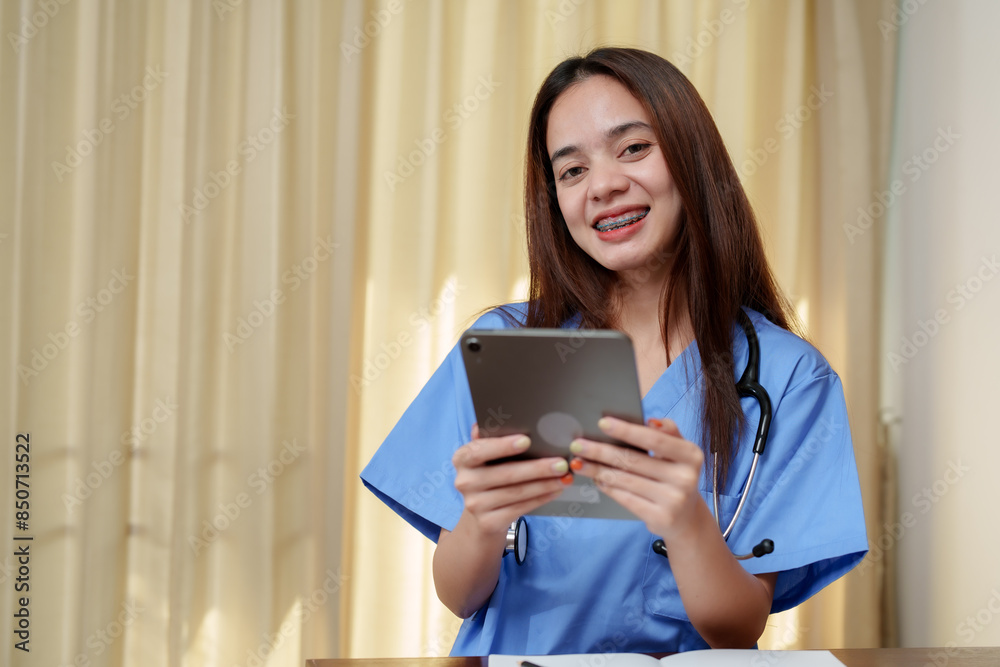 Asian girl with braces and glasses, wearing blue scrubs, holding tablet, smiling. Home setting with focus on cheerful expression and medical student lifestyle. Warm lighting enhances cozy atmosphere. Asian girl with braces and glasses, wearing blue scrubs, holding tablet, smiling. Home setting with focus on cheerful expression and medical student lifestyle. Warm lighting enhances cozy atmosphere.
