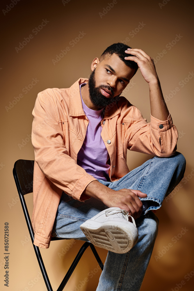 Obraz premium Handsome African American man sitting in a chair, hand on head, contemplating.