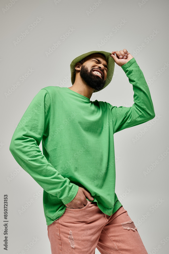 Fototapeta premium Stylish African American man with beard in green hat posing on vibrant backdrop.