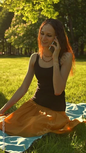 Front view of a woman sitting towards camera talking during a selfphone calling her friend in the park Vertical shot. photo