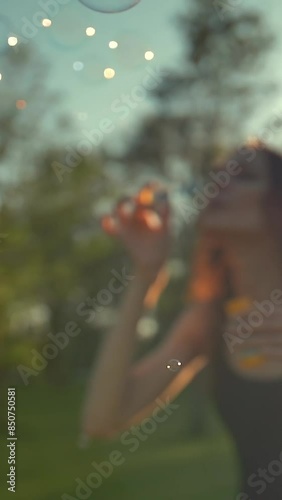 Portrait of beautiful redhair young woman. Blowing bubble in the park. Super slow motion shot in 180 fps. Sunset straight orange light. Vertical shot.