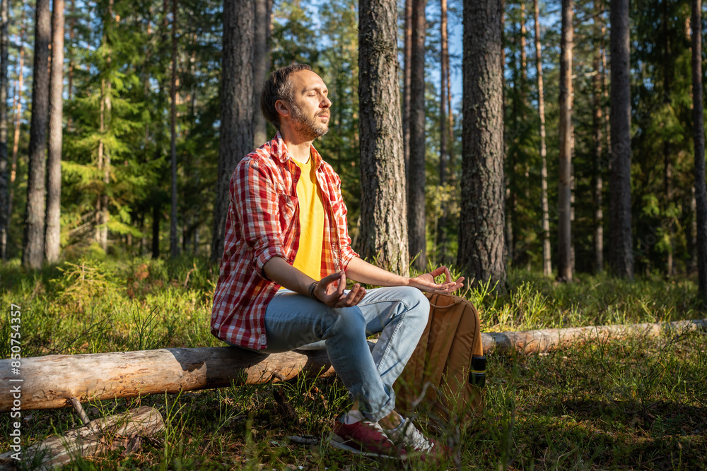 Man meditates in woods at fresh forest air. Middle aged male sits on fallen tree immerses in sounds of nature and foliage, uses special breathing technique, spiritually relaxes, unloading thoughts Man meditates in woods at fresh forest air. Middle aged male sits on fallen tree immerses in sounds of nature and foliage, uses special breathing technique, spiritually relaxes, unloading thoughts