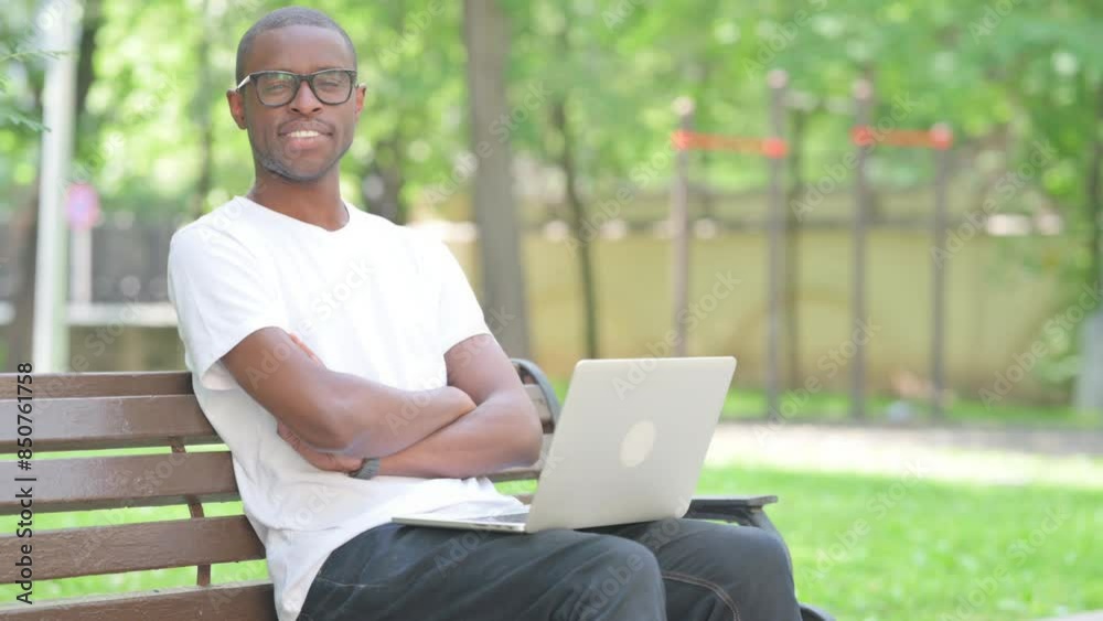 Young African Man Smiling at Camera while Using Laptop Outdoor Young African Man Smiling at Camera while Using Laptop Outdoor