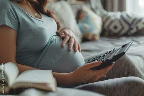 Pregnant woman using a calculator in the style of agini concept, a pregnant female holding her stomach sitting on a sofa at home with a notebook and digital renderer near her belly photo