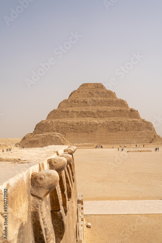 The step pyramid of Djoser In Saqqara, Egypt with stone carved cobra snakes in the foreground photo