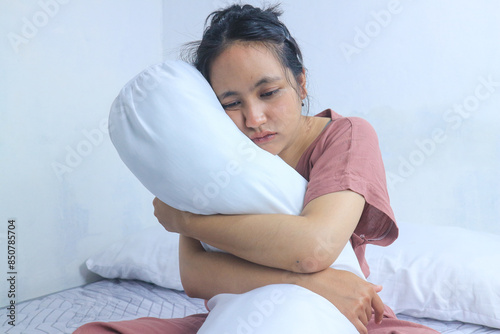 Tired sad and sick facial expression of beautiful woman insomnia in bedroom, hugging bolster photo