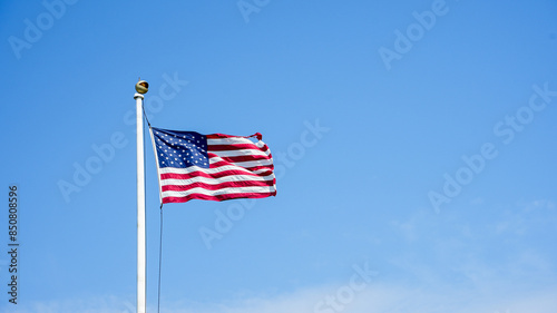A photograph of the American flag waving proudly in the wind against a backdrop of a clear blue sky.