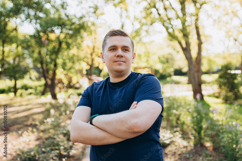 Outdoor portrait of confident smiling happy man of 30 years. Positive handsome male with arms crossed in blue t-shirt in the city park. Outdoor portrait of confident smiling happy man of 30 years. Positive handsome male with arms crossed in blue t-shirt in the city park.