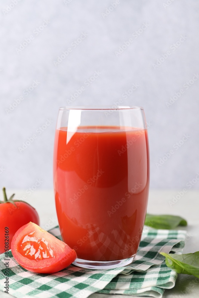 Tasty tomato juice in glass, basil leaves and fresh vegetables on light table Tasty tomato juice in glass, basil leaves and fresh vegetables on light table