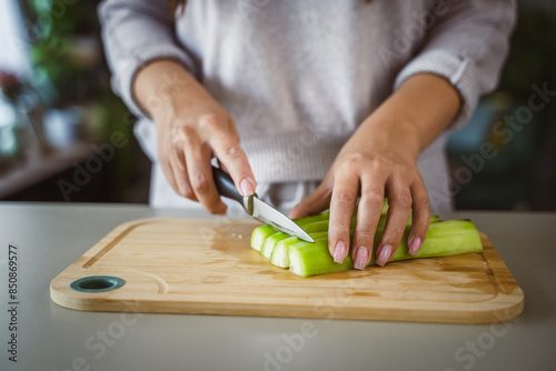 An unknown adult caucasian woman stand and cut cucumber at home