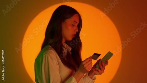 Stylish young woman in casual clothing typing credit card number in smartphone app. Isolated on colorful studio background yellow spotlight. photo