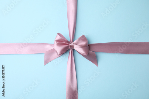 Pink satin ribbon with bow on light blue background, top view © New Africa