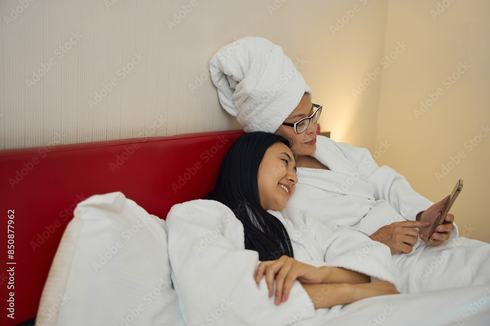 Family of two whiling away time with smartphone in bedroom Family of two whiling away time with smartphone in bedroom