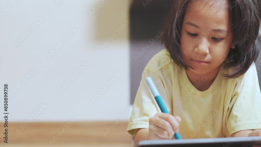 Adorable asian kid girl, drawing or writing on a tablet, lies on the floor of a cozy room. It shows the modern technology and creativity in early education of child for learning and development. Adorable asian kid girl, drawing or writing on a tablet, lies on the floor of a cozy room. It shows the modern technology and creativity in early education of child for learning and development.