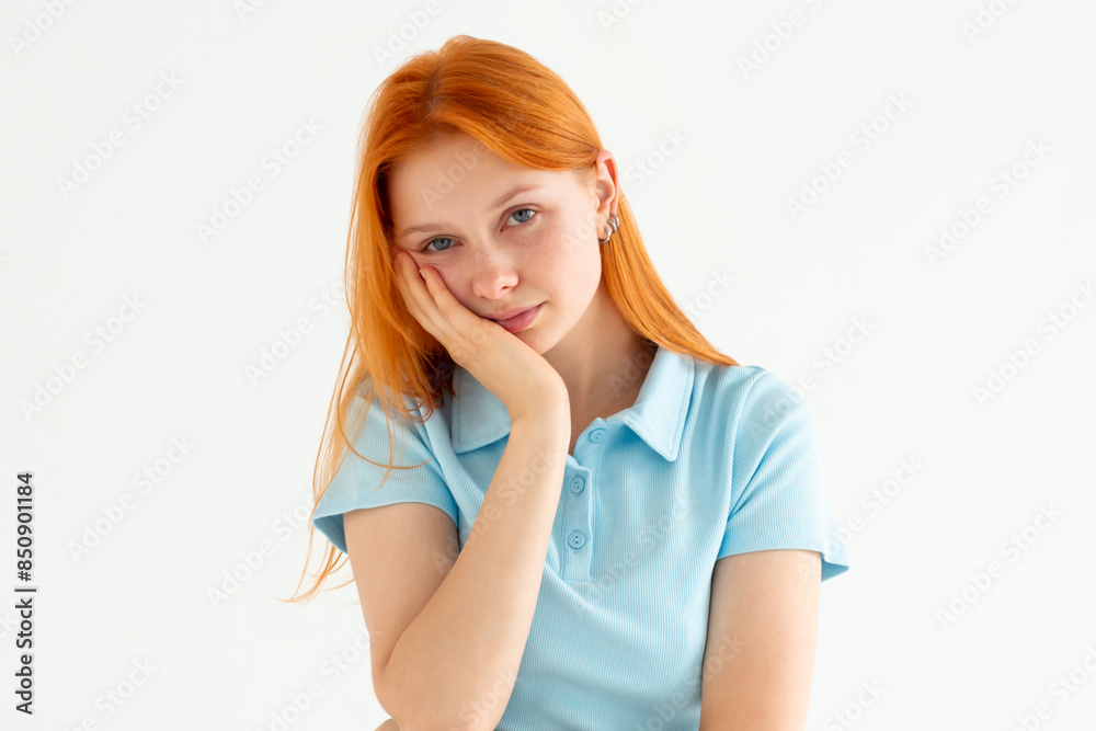 Cute redhead woman standing in blue t-shirt, holding palm on cheek and leaning face on it, being bored and tired of uninteresting talks, feeling indifferent to what happening over white wall Cute redhead woman standing in blue t-shirt, holding palm on cheek and leaning face on it, being bored and tired of uninteresting talks, feeling indifferent to what happening over white wall
